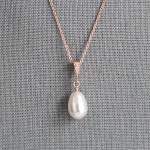 May include: A rose gold necklace with a single large pearl pendant. The pendant is attached to a delicate chain with a small cluster of clear cubic zirconia stones.