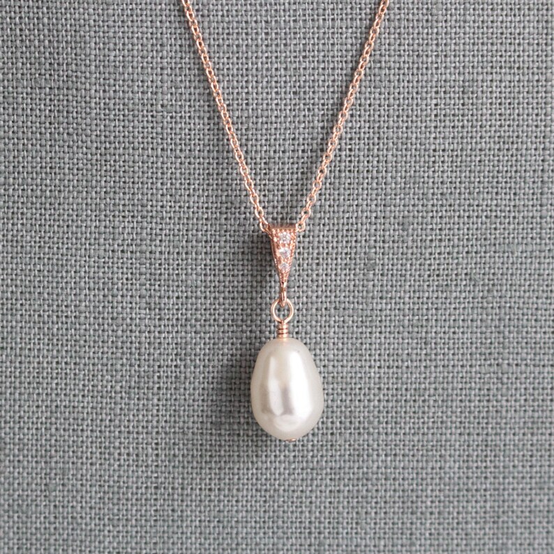 May include: A rose gold necklace with a single large pearl pendant. The pendant is attached to a delicate chain with a small cluster of clear cubic zirconia stones.