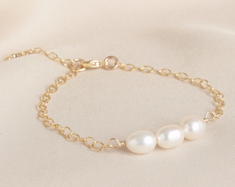 May include: A delicate gold chain bracelet featuring three white pearls. The bracelet has a lobster clasp fastening.