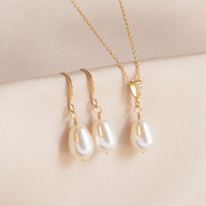 May include: A set of gold pearl jewellery featuring a necklace and a pair of earrings. The necklace has a delicate gold chain with a small pearl pendant. The earrings are drop earrings with a single pearl on each.