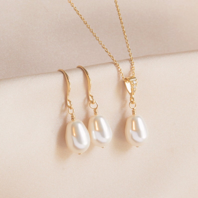 May include: A set of gold pearl jewellery featuring a necklace and a pair of earrings. The necklace has a delicate gold chain with a small pearl pendant. The earrings are drop earrings with a single pearl on each.