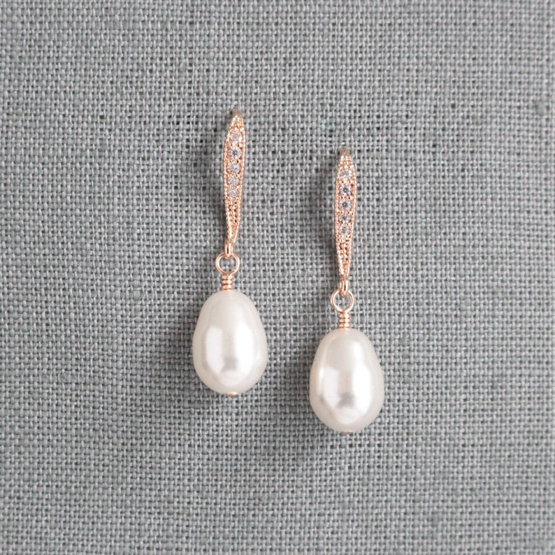 May include: A pair of rose gold earrings with a teardrop-shaped pearl and a crystal-encrusted dangle.