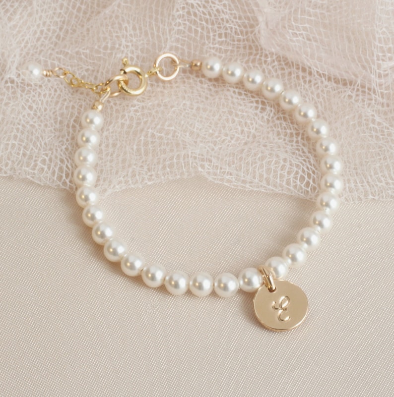 May include: A delicate pearl bracelet with a gold charm featuring the letter "E". The bracelet is made of small, white pearls and has a gold clasp.