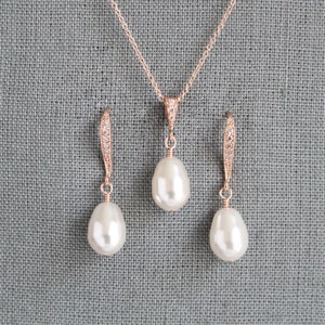 May include: A rose gold necklace and earrings set with a teardrop shaped pearl pendant and matching earrings. The necklace and earrings are adorned with small clear cubic zirconia stones.