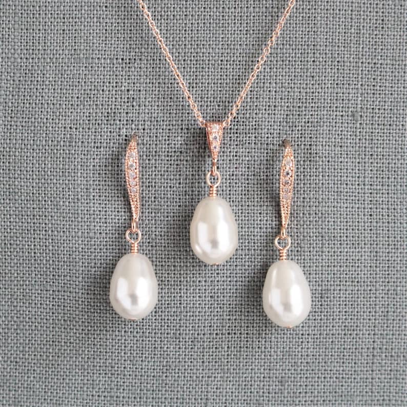May include: A rose gold necklace and earrings set with a teardrop shaped pearl pendant and matching earrings. The necklace and earrings are adorned with small clear cubic zirconia stones.