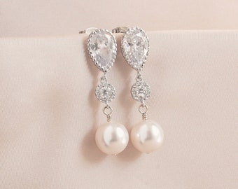 May include: A pair of silver dangle earrings with pear-shaped clear crystal stones, round crystal accents, and white pearl drops.