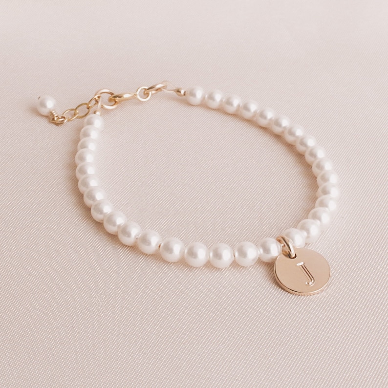 May include: A delicate pearl bracelet with a gold charm featuring the letter "J".