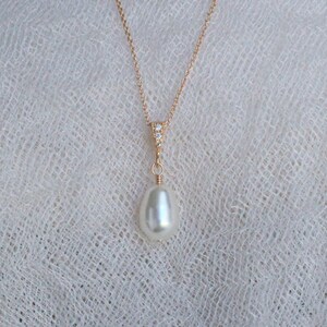 May include: A delicate gold chain necklace with a single, large, white pearl pendant. The pendant is accented with a small cluster of clear cubic zirconia stones.