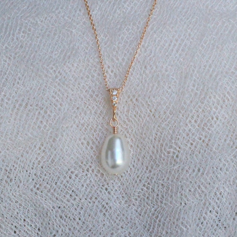 May include: A delicate gold chain necklace with a single, large, white pearl pendant. The pendant is accented with a small cluster of clear cubic zirconia stones.