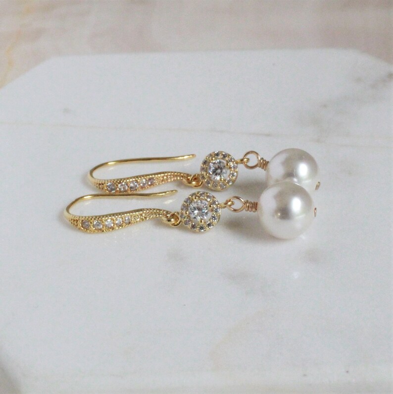 May include: A pair of gold earrings with a pearl and a small round rhinestone setting. The earrings have a delicate, dangling design.