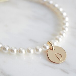 May include: A delicate pearl bracelet with a gold charm featuring the letter 'D'.