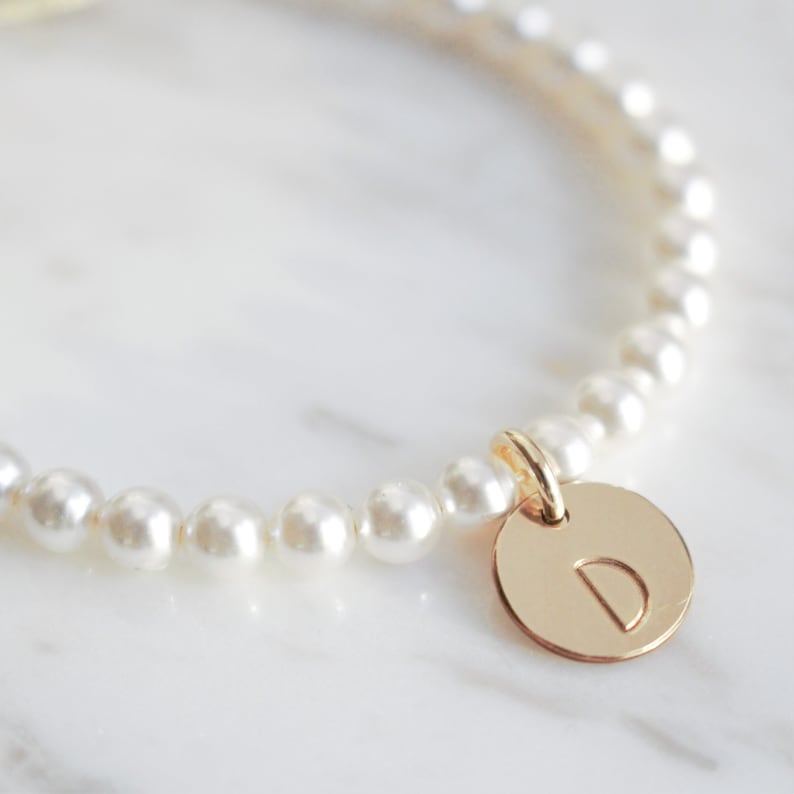 May include: A delicate pearl bracelet with a gold charm featuring the letter 'D'.