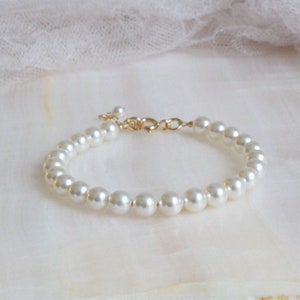May include: A simple gold chain bracelet with white faux pearls. The bracelet is made of small, round pearls that are evenly spaced along the chain.