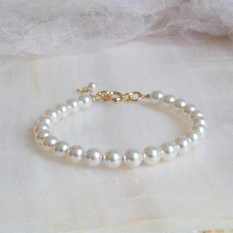 May include: A simple gold chain bracelet with white faux pearls. The bracelet is made of small, round pearls that are evenly spaced along the chain.