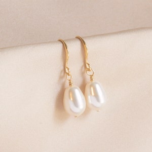 May include: A pair of gold drop earrings with white pearl accents. The earrings have a simple, elegant design.