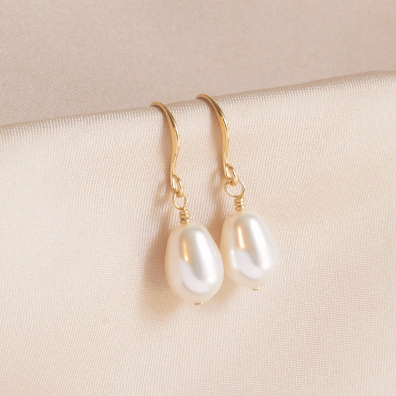 May include: A pair of gold drop earrings with white pearl accents. The earrings have a simple, elegant design.