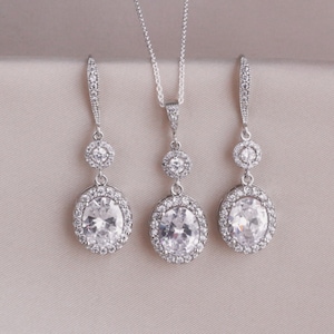May include: A silver necklace and earrings set with large oval-shaped clear cubic zirconia stones surrounded by smaller stones.