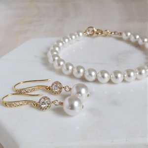 May include: A set of pearl jewelry featuring a gold chain bracelet with white pearls and a pair of gold earrings with white pearls and clear rhinestones.