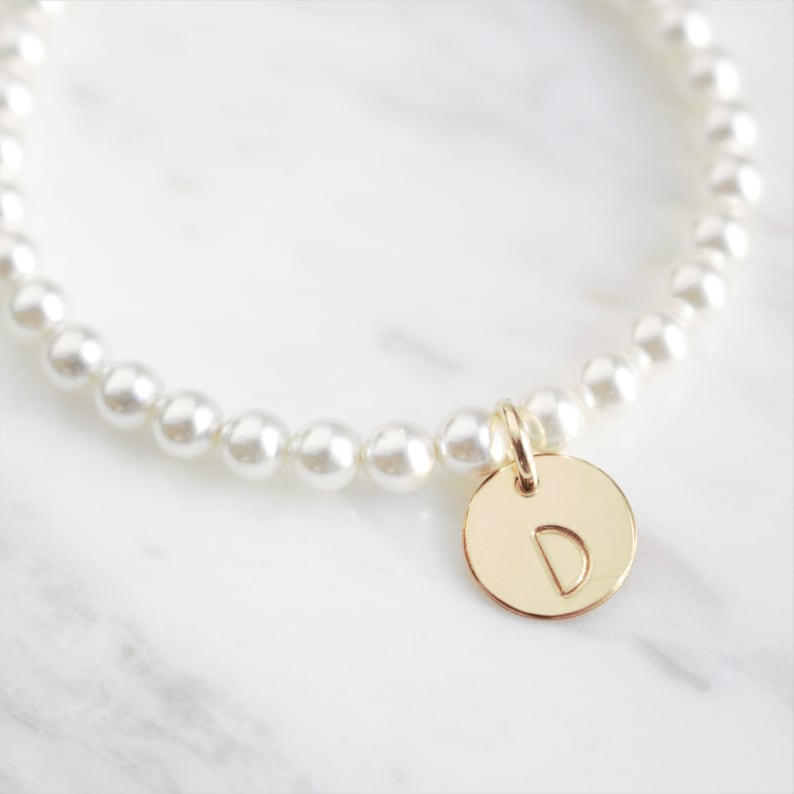 May include: A white pearl bracelet with a gold charm featuring the letter 'D'.