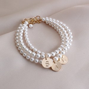 May include: A layered pearl bracelet with three gold charms, each with a different letter: S, I, and L.