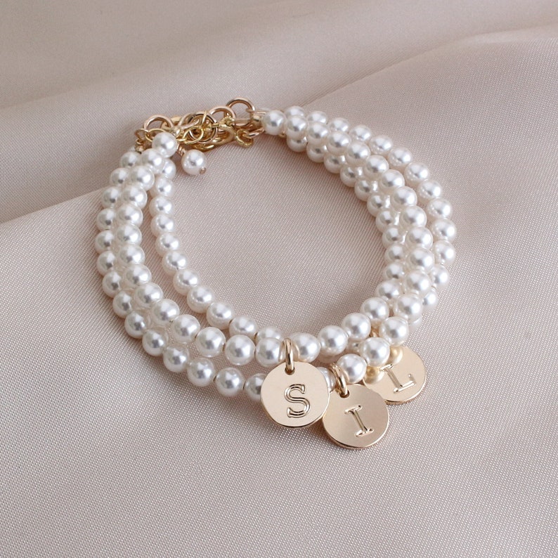 May include: A layered pearl bracelet with three gold charms, each with a different letter: S, I, and L.