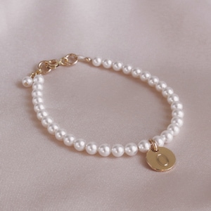 May include: A delicate pearl bracelet with a gold charm featuring the letter "O".