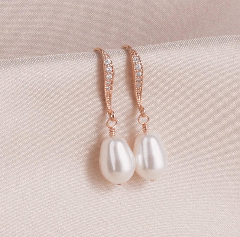May include: A pair of gold earrings with a pearlescent drop and a row of clear cubic zirconia stones.