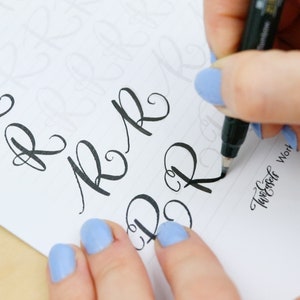 May include: A person practicing calligraphy with a black marker pen on a white sheet of paper. The paper has faint guidelines for the letters. The person is writing the letter "R" in cursive. The text "Twirler Work" is written in cursive at the bottom of the page.