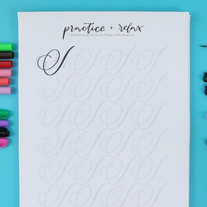 May include: A white sheet of paper with the text "practice + relax" at the top. The paper has a grid of cursive "S" shapes for practicing calligraphy. There are various pens and markers on a blue surface next to the paper.