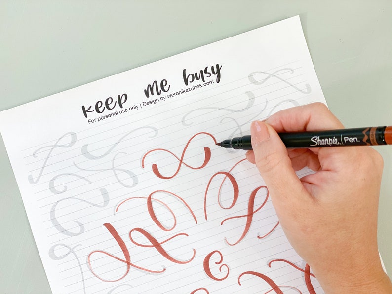 K&ouml;nnte beinhalten: Eine Hand h&auml;lt einen braunen und schwarzen Markierstift mit der Aufschrift "Sharpie Pen". Die Hand schreibt auf ein Blatt Papier mit grauen Linien. Das Papier hat oben die Worte "keep me busy" geschrieben. Die Worte sind in schwarzer Tinte geschrieben. Die Hand schreibt in kupferfarbener Tinte.