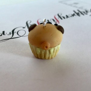 Pu&ograve; includere: Un piccolo cupcake marrone e giallo con gocce di cioccolato sulla cima. Il cupcake ha un buco al centro della parte superiore e un anello d'argento per appenderlo.