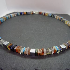 May include: A multi-colored gemstone necklace with square and rectangular beads. The necklace is made of various stones, including turquoise, carnelian, amethyst, and hematite.