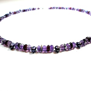 May include: A purple and black beaded necklace with amethyst, garnet, and pearl beads.