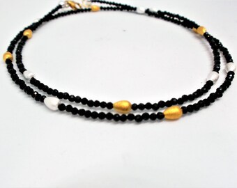 Puede incluir: Un collar de doble cadena con cuentas negras y detalles dorados y plateados.