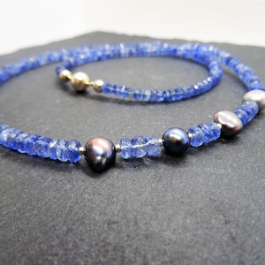 May include: A blue sapphire and black pearl necklace with silver and gold accents. The necklace is made of small, faceted sapphire beads and features three large black pearls.