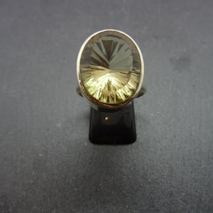 Könnte beinhalten: Ein silberner Ring mit einem großen, ovalen, facettierten, hellgrünen Edelstein.