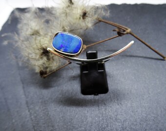 May include: A silver ring with a blue opal gemstone set in a curved band.