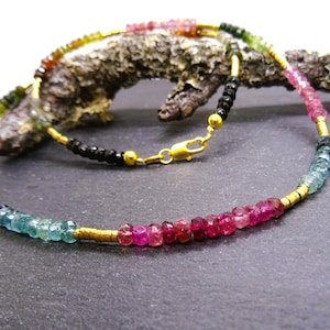 May include: A multi-colored gemstone necklace with gold beads and a clasp. The necklace features pink, green, and blue gemstones.