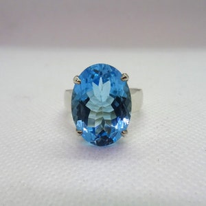 May include: A silver ring with a large oval-shaped blue topaz gemstone.