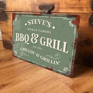 May include: A green metal sign with a rustic look, featuring the text "Steve's World Famous BBQ & Grill Est. 2024 Chillin' & Grillin'" in white lettering.