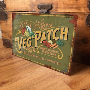 May include: A green metal sign with the text "Jessie's Veg Patch" in yellow and orange letters. The sign also includes the text "Where beautiful things begin" and "Trespassers will be composted". The sign features a colourful illustration of vegetables.