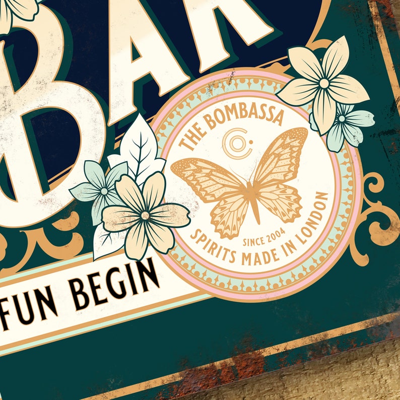 Pu&ograve; includere: Un cartello in stile vintage con il testo "The Bombassa Spirits Made in London Since 2004" in un cerchio con un design a farfalla. Il cartello ha uno sfondo verde con accenti dorati e il testo "Fun Begin" in basso.
