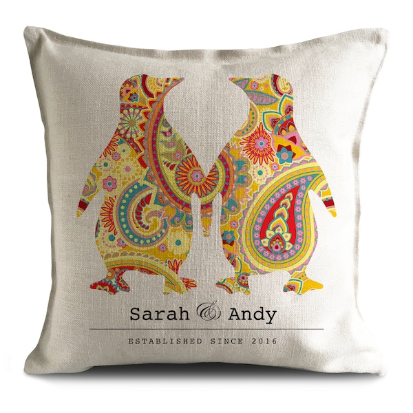 Op de afbeelding: Een wit kussen met twee gestileerde pinguïns die elkaar aankijken. De pinguïns zijn gevuld met een kleurrijk paisley-patroon in tinten geel, rood, blauw en groen. De tekst "Sarah & Andy Established Since 2016" is onder de pinguïns gedrukt.