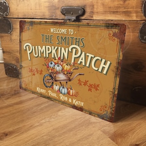 May include: A rectangular metal sign with a vintage design. The sign reads "Welcome to The Smiths Pumpkin Patch" with a wheelbarrow filled with pumpkins. The sign is in shades of orange, brown, and green, with the names Kerry, Paul, Rob & Katie.
