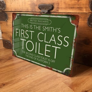 May include: A green metal sign with white text that reads "BRITISH RAILWAYS THIS IS THE SMITH'S FIRST CLASS TOILET THE SECOND CLASS TOILET IS OFF THE END OF PLATFORM 3".