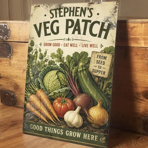 May include: A rectangular metal sign featuring the words "STEPHEN'S VEG PATCH" and illustrations of vegetables. The sign includes carrots, a tomato, garlic, an onion, a cabbage, a courgette, and beetroot. The text "GROW GOOD - EAT WELL - LIVE WELL" is also present.