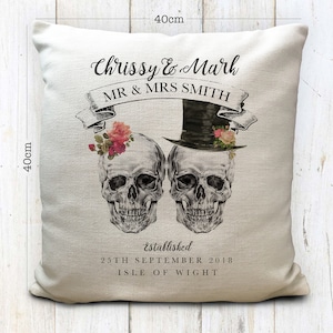 May include: A white cushion with a black and white illustration of two skulls wearing a top hat and flowers. The text "Chrissy & Mark MR & MRS SMITH established 25TH SEPTEMBER 2018 ISLE OF WIGHT" is printed on the cushion.