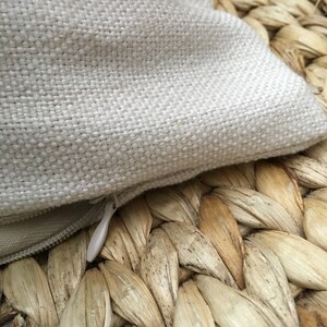 May include: A close-up of a white pillowcase with a zipper closure. The pillowcase is made of a soft, woven fabric and is lying on a woven wicker surface.