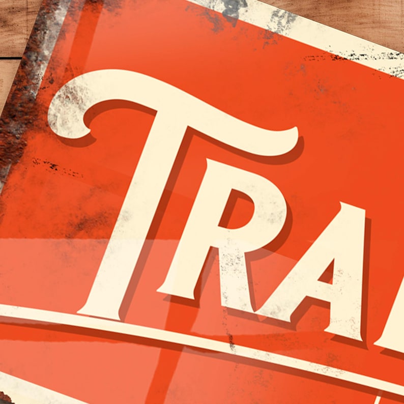 Op de afbeelding: Een vintage metalen bord met een rode achtergrond en witte letters. Het bord heeft de tekst "TRADE". Het bord heeft een verweerde, roestige uitstraling.