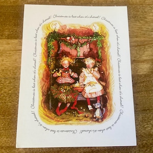 May include: A Christmas card featuring an illustration of two children near a fireplace. One child wears a red and white striped top and green skirt, the other wears a white apron. The text "Christmas is best when it's shared!" is written around the border.